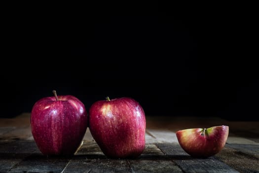 Red tasty wet apple on a wooden table. Black background.