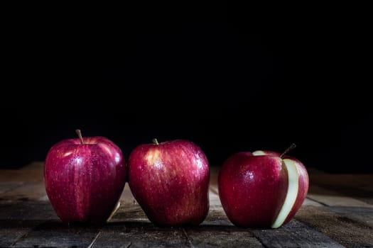 Red tasty wet apple on a wooden table. Black background.