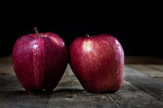 Red tasty wet apple on a wooden table. Black background.