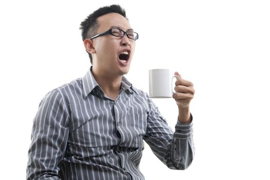 Yawning Asian male holding a cup of coffee isolated on white background