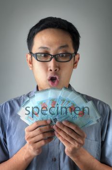 A Malaysian man holding Ringgit Malaysia currency with surprising face expression, isolated on grey background.