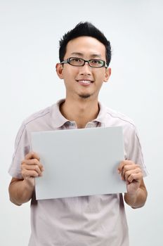 Casual Asian male displaying a grey empty card, standing isolated on grey background.