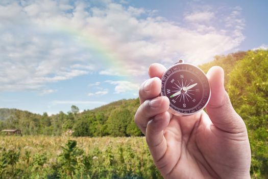 Compass in hand on blur of mountain view with rainbow for background