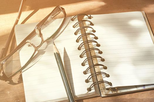 Empty page of notebook on desk, Black pencil and glasses on notebook, Space for text, Vintage style