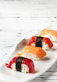  Set of salmon and red tuna Nigiris on white plate over old white wood. Raw fish in traditional Japanese sushi style. Vertical image.