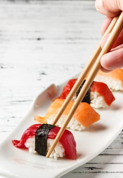  Set of salmon and red tuna Nigiris on white plate over old white wood with chopsticks. Raw fish in traditional Japanese sushi style. Vertical image.