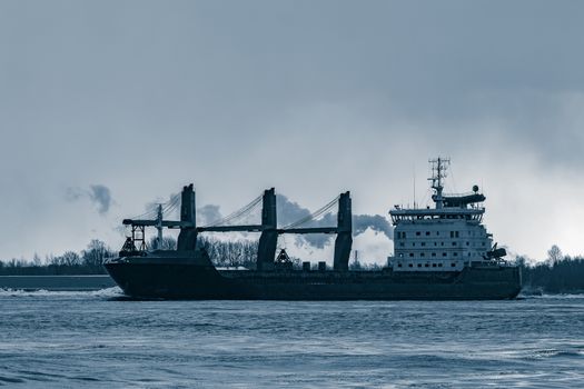 Blue bulk carrier sailing to the sea in cold winter. Monochrome
