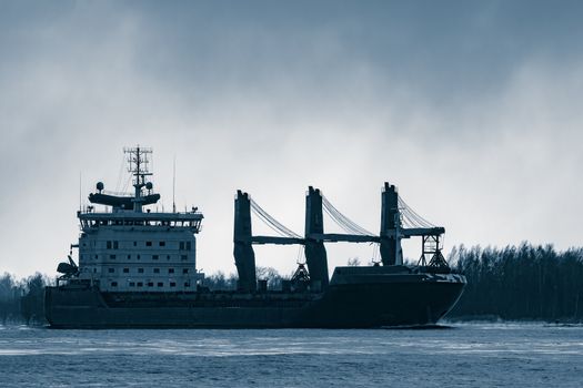Blue bulk carrier sailing to the sea in cold winter. Monochrome