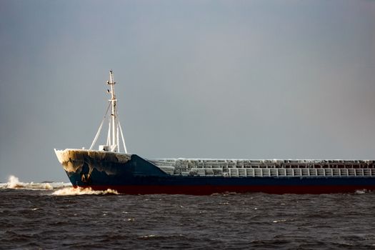 Blue bulk carrier moving from the sea in cold winter
