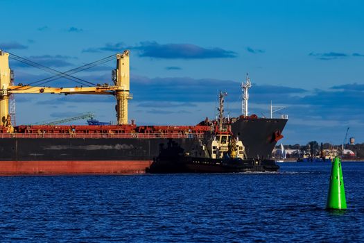 Black cargo ship mooring at the port with tug ship support