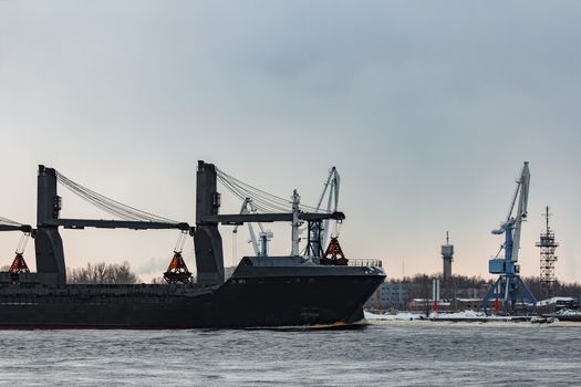 Black bulk carrier sailing to the sea in cold winter