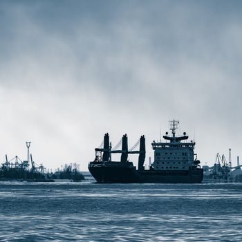 Blue bulk carrier sailing to the sea in cold winter. Monochrome