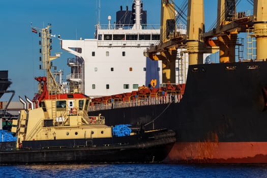 Black cargo ship mooring at the port with tug ship support