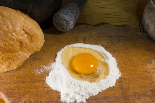 Broken egg in flour on a wooden cutting board