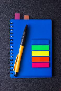 Blue notepad with multi-colored stickers and pen on a black background