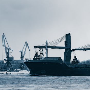 Blue bulk carrier sailing to the sea in cold winter. Monochrome