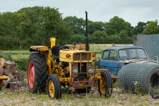 Old, rusting, yellow tractor on waste ground.