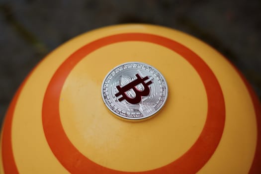 Digital currency physical red bitcoin coin on yellow circle background.