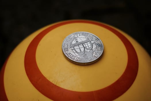 Digital currency physical silver bitcoin coin on yellow circle background.