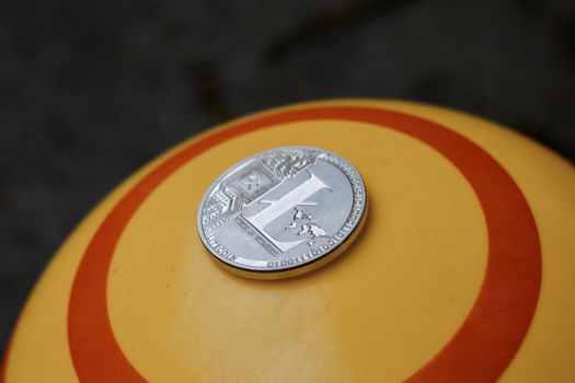 Digital currency physical silver litecoin coin on yellow circle background.