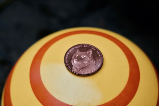 Digital currency physical brass dogecoin coin on yellow circle background.