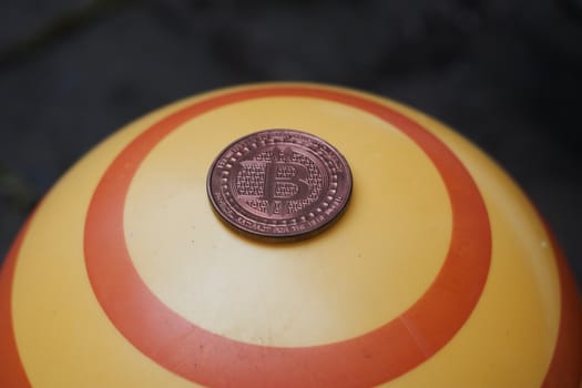 Digital currency physical brass bitcoin coin on yellow circle background.