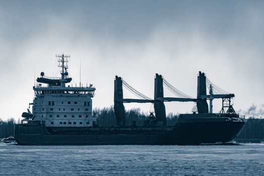 Blue bulk carrier sailing to the sea in cold winter. Monochrome