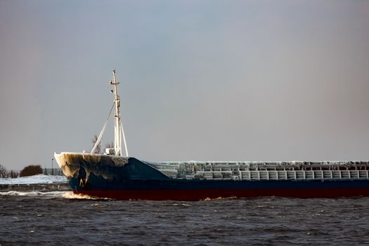 Blue bulk carrier moving from the sea in cold winter