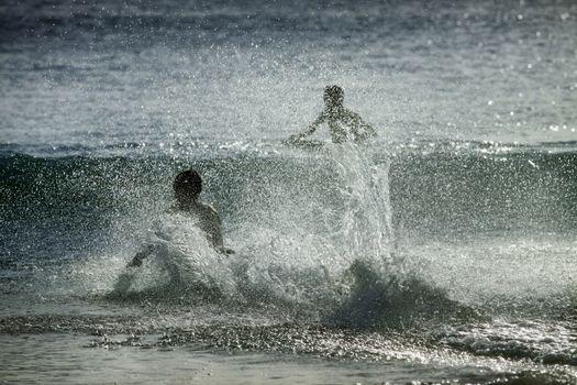 Silhouettes of people in the splashes of the ocean at sunset