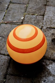 Big yellow ball with red stipes around on the stone floor in garden.