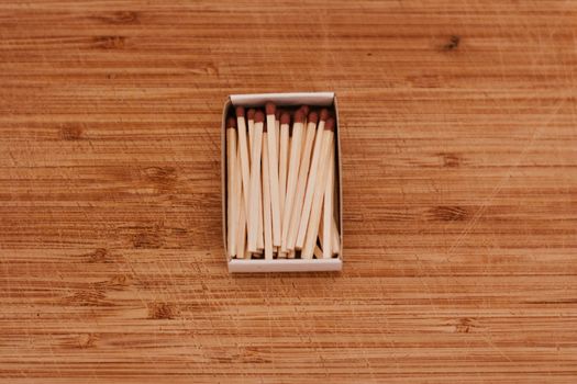 Small wooden matches in a box on the wooden board. Closeup photography.