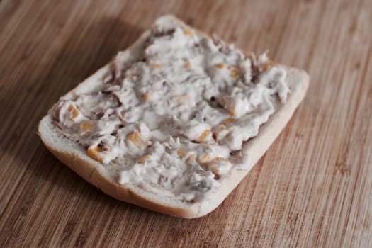Tasty and fresh sandwich with tuna, butter and sweetcorn on the wooden board in the kitchen.