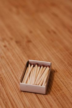 Small wooden matches in a box on the wooden board. Closeup photography.