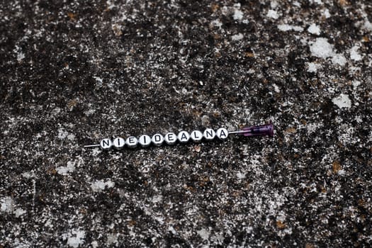 Small silver letters on the needle in dirty dark background. Nieidealna.