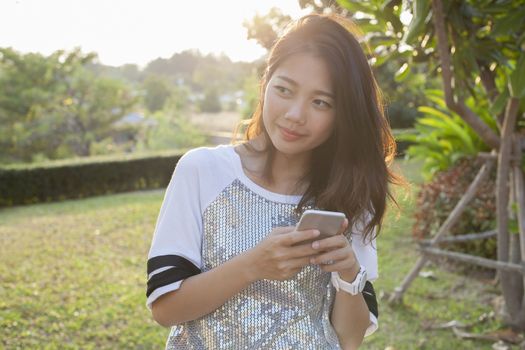 asian younger woman with smartphone in hand happiness thinking ,relaxing outdoor