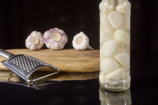 Marinated and fresh garlic with a grater on a dark background