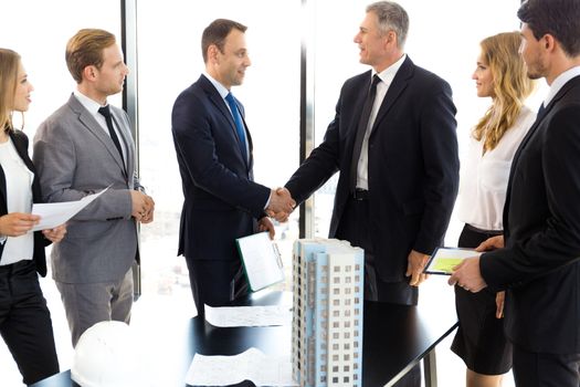 Business meeting of architects and investors shaking hands finishing deal, model of modern multi storey residential building house on table