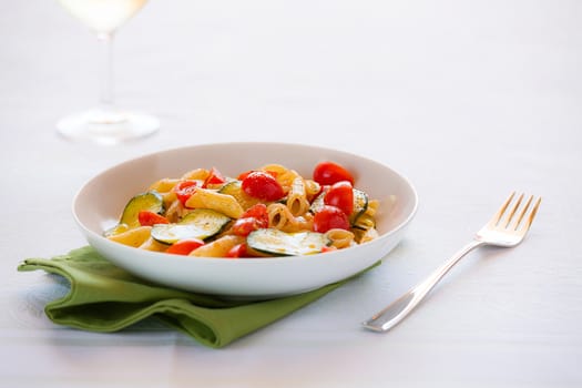 Traditional italian penne pasta with zucchini and cherry tomatoes seasoned with oil and black pepper