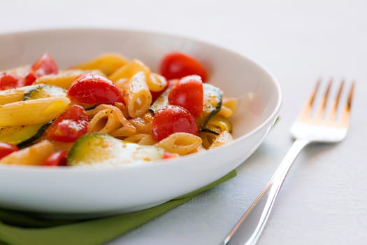 Closeup of traditional italian penne pasta with zucchini and cherry tomatoes seasoned with oil and black pepper