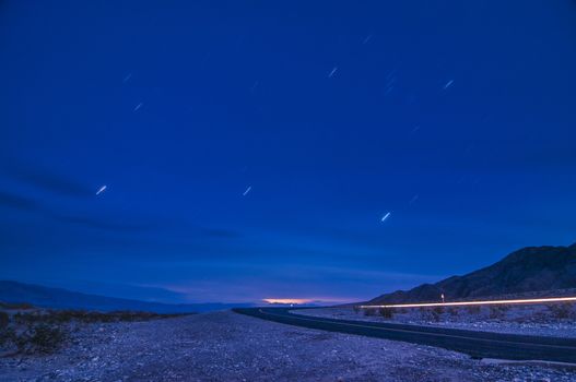 Moonlit road with car's headlight trails and star-trails in Death Valley, California