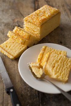 Slices of a fresh cake with lemon icing served on a side plate with a fork viewed high angle on a rustic wooden table