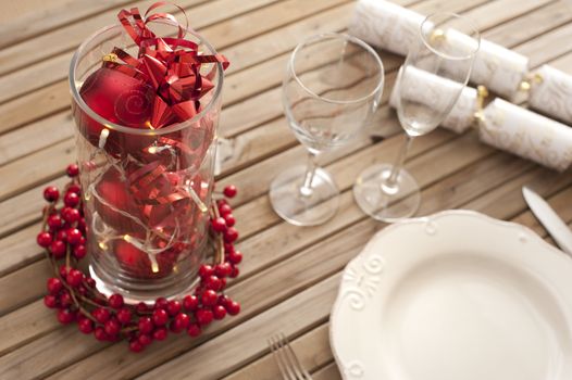 Christmas table setting with red decorations and berries on a slatted wood table ready to celebrate the holiday season