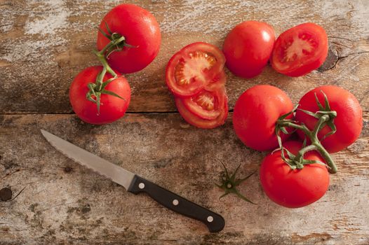 Preparing fresh tomatoes for a salad or cooking with an overhead view of ripe cherry tomatoes and a kitchen knife on an old chopping board