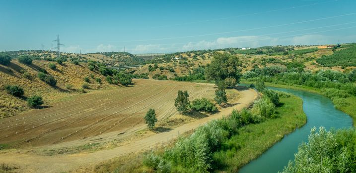 Grass meadow on the spanish countryside of Cordoba with electricity tower pole in the background and a stream flowing by in Spain,Europe on a bright sunny day with blue sky