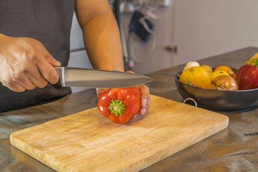 Chef cutting red bell pepper on wooden broad.