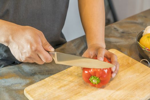 Chef cutting red bell pepper on wooden broad