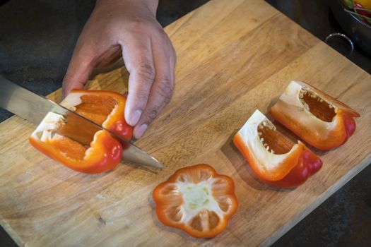 Chef cutting red bell pepper on wooden broad.