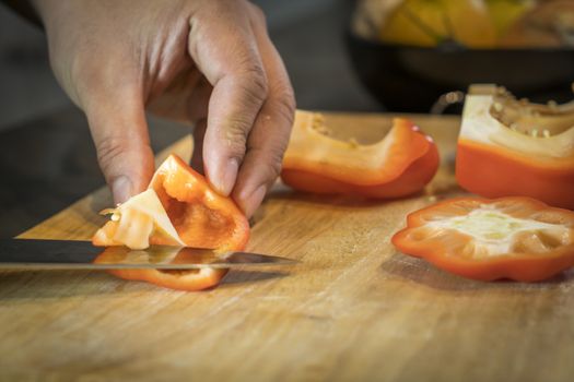 Chef cutting red bell pepper on wooden broad.