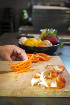 Chef cutting red bell pepper on wooden broad.