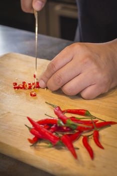 Hand slicing Chilli pepper with Knife on chopping board on wooden background.